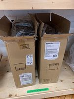 Two cardboard boxes labeled Kichler Serca 3-light flush mount fixtures on wooden shelf