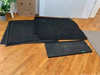 Seven black carpet floor mats spread on hardwood floor with boot tray alongside