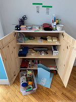 Office supplies stored inside and on top of a wooden cabinet with open doors showing paper pads, containers, and various small items.