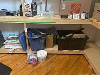 Photo of shelving with plastic bins containing various plumbing supplies, pipes, and some other boxes and supplies on shelves and floor