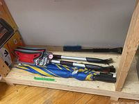 Three IKEA golf umbrellas folded on a wooden shelf next to two snow brushes and one snow brush/ice scraper, showing general lot content.