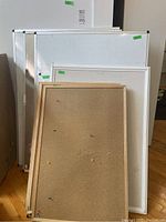 Set of three wood framed pinboards leaned in front of multiple whiteboards of various sizes, showing wood frame details and push pin holes on pinboards.