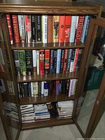 Full view of a wooden cabinet with three shelves filled with hardcover books, showing various titles and colors.
