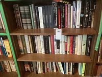 Books arranged in three rows on wooden shelves showing mixed genre collection of hardcover and softcover books