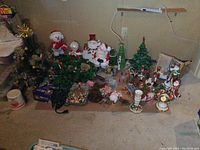 Wide view of all Christmas decorations arranged on the ground including two trees and multiple figurines and ornaments.