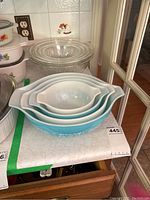 Stack of four turquoise Pyrex Butterprint mixing bowls nested together with six clear Corning glass bowls behind