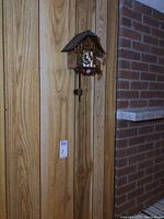 Full view of vintage cuckoo clock hanging on wood wall with pendulum and weights clearly visible