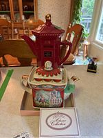 Front view showing London Pottery post box teapot and Sadler Romeo and Juliet teapot with booklet on table.