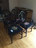 Four dark wood dining chairs with shield backs and needlepoint floral seats arranged with two arm chairs and two side chairs visible.