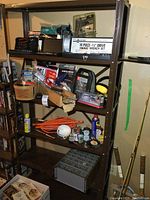 View of entire metal shelving unit containing various hand tools, socket sets, lubricants, hardware, organizer boxes, extension cord, saws, stapler, glue gun, and other miscellaneous items.