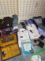 Photo showing men's dress shirts, ties, cuff links in wooden box, wallets, watch and sunglasses spread out on floor