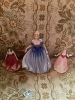 Group photo of three porcelain ladies figurines seated on floral upholstery background.