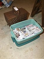 View of vintage wood fold out sewing box next to a large green plastic tote bin containing sewing patterns.