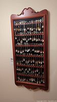 Full view of wooden spoon display case mounted to wall filled with multiple rows of souvenir spoons.
