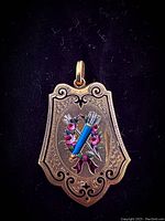 Frontal view of shield-shaped pendant locket with engraved border and hand-painted enamel quiver, arrows, and rose motif
