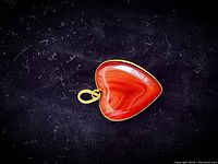 Front view of heart-shaped carnelian pendant set in 22kt yellow gold on a dark background
