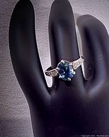 Oblique view of ring on display hand showing oval sapphire color and side profile of setting