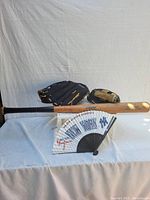 Baseball bat placed horizontally with two baseball gloves behind and a New York Yankees fan in front, displayed on white fabric background.