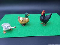 Three painted cast lead ducks and a black hen on green background