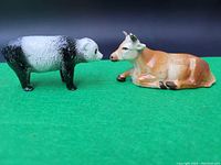 Black and white sheep and brown and white reclining cow figurines on green surface