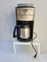Front view of Cuisinart coffee maker with digital control panel and stainless steel thermal carafe on white stand.
