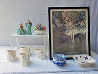 Overview of lot showing porcelain figurines, napkin rings, vase, small blue pot, oval porcelain bowl, and framed print