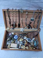 Open cedar box displaying assortment of costume jewelry including necklaces, bracelets, pins, and small accessories.