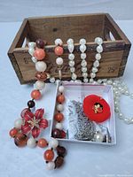 Photo showing small wooden mini Coke crate with various costume jewelry including beaded necklaces and pins inside and around it.