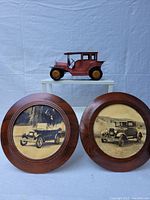 Front view of two circular wooden framed Ford Model T black-and-white photographs and Ford Model T replica on a white stand