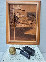 Framed wood carving showing a golfer mid-swing near hole 10 flag, displayed on a white perforated surface with other golf-related items below.