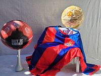 Two soccer balls and a red and blue striped football shirt displayed together