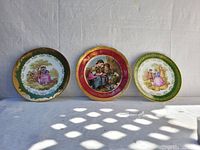 Front view of the three La Mouve collectible Limoges porcelain plates showing the artwork and gilded edges.