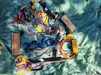 Photo showing a variety of hand tools and accessories spread out on a green tarp including clamps, staplers, pliers, tape measure, an extension cord, gloves, and small tools