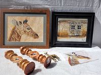 Overall view of framed giraffe and barn paintings with wooden objects and brass giraffe figurine arranged on white cloth.