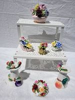 Front view of seven decorative porcelain floral pieces placed on a white perforated stand and flat surface.