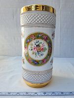 Front view of the tall cylindrical porcelain vase showing floral design, lattice pattern, and gold trim.