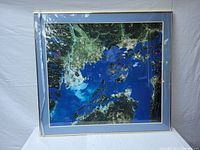 Photo of framed satellite image showing the Lower Mainland area with land and water bodies, within a clear light-colored frame.