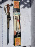 Photo of the sword and pistol replica packaged in a box labeled 'Hunting Sword Pistol' with information about authentic appearance and shell guns.