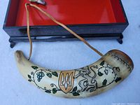 Powder horn outside the box showcasing painted Ukrainian lion and trident symbols along with vine patterns.