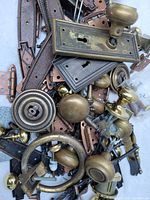 Close-up of vintage mixed metal hardware including brass knobs, backplates, and hinges with visible patina and wear.