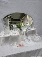 Full view of the vintage oval mirror standing behind various cut crystal glassware pieces placed on white stands and table.