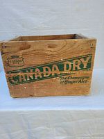 Front view of vintage wooden Canada Dry soda crate with green logo and slogan.