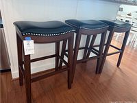 Three bar stools side by side showing full front view of black seats, nailhead trim and wooden legs