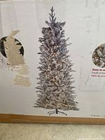 Box photo showing image of 7.5 ft snowflecked artificial Christmas tree with stand, illustrating tree size and appearance.