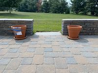 Two large terracotta planters with matching saucers sitting on stone patio with grass backdrop.