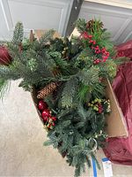 Photo of faux spruce garland showing pine cones and red berries bundled inside a cardboard box.