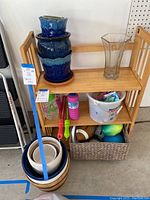 View of the shelving unit and floor showing blue ceramic pots stacked on top, bubble toys, goggles, and a basket with sports balls underneath.