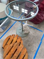 Full view of the metal and glass round decorative table with bunny and bird motif alongside the two wooden wheeled plant stands.