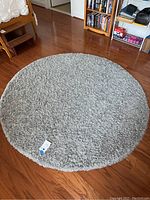 Full top view of the round grey shag rug on hardwood floor near bookshelf and chair.