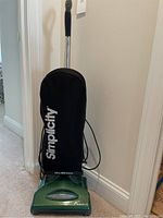 Full view of the green Simplicity Freedom vacuum cleaner upright with black cloth bag and handle visible.